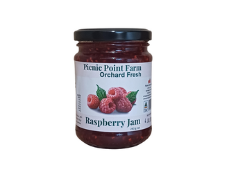 A clear glass jar of jam with a white label and raspberries pictured. The product has a black lid.